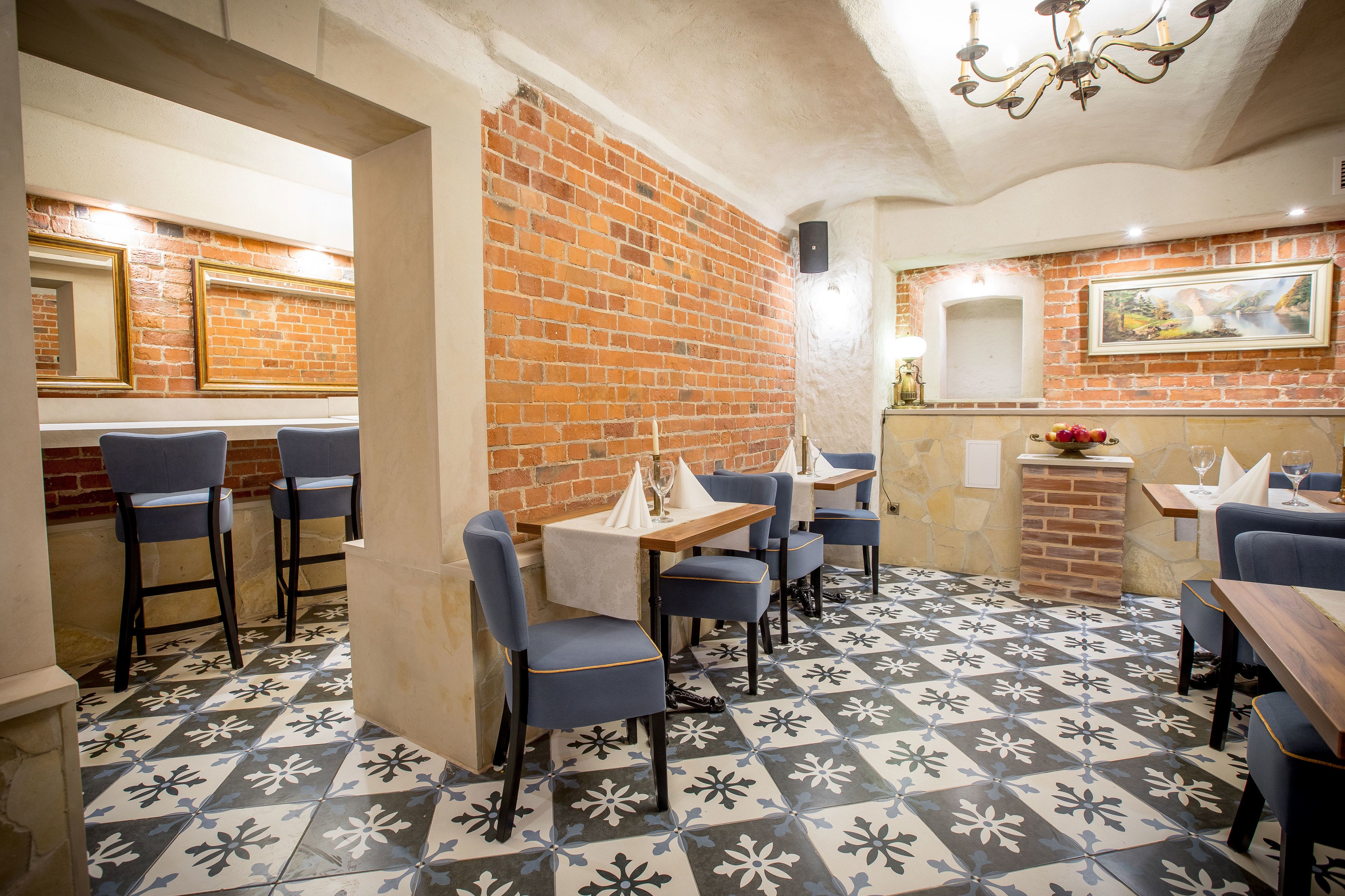 A restaurant interior with brick walls, blue chairs, and patterned floor tiles.
