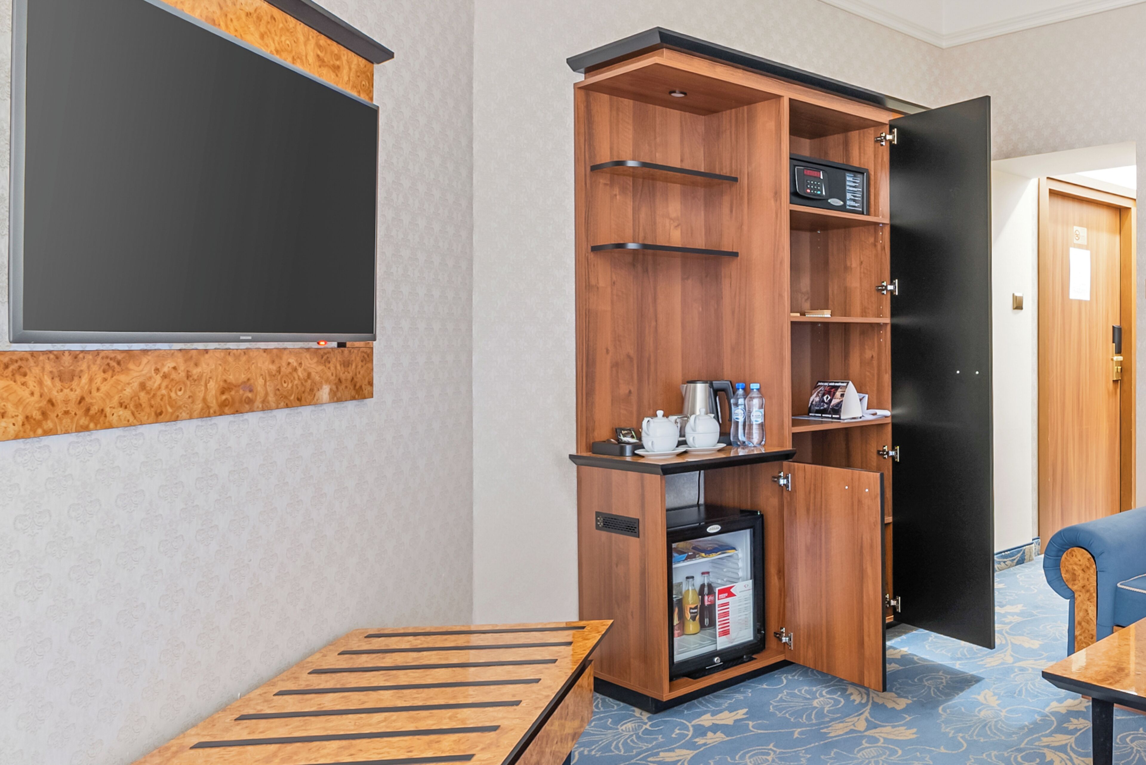 Une chambre d’hôtel équipée d’un meuble en bois contenant une machine à café, un service à thé et des bouteilles d’eau.