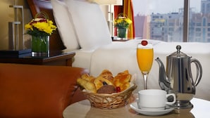 A hotel room with a breakfast setup including bread, a glass of orange juice, a coffee pot, and a vase with flowers. - Al Safir Hotel & Tower (Manama)