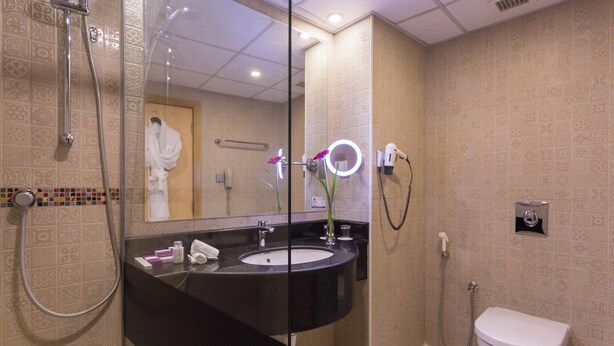A bathroom with a large mirror, a sink, a toilet, and a shower. - Al Safir Hotel & Tower (Manama)