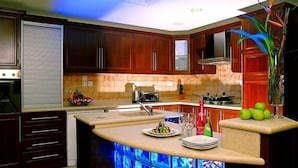 A modern kitchen with wooden cabinets, a built-in island with blue lighting, and a decorative plant. - Al Safir Hotel & Tower (Manama)