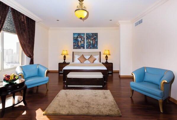 Ein Schlafzimmer mit einem großen Bett, zwei blauen Sesseln, einem runden Tisch mit Obst und zwei Lampen.