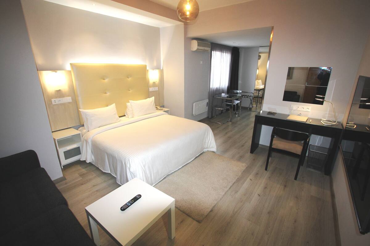 A hotel room with a large bed, bedside tables, a desk, a chair, and a TV.