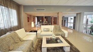 Een ruime lobby met een modern design, met een zithoek met twee banken en een salontafel, een receptiebalie en een uitzicht op buiten door grote ramen.