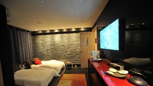 Een moderne kamer met een stenen muur, een bed met wit beddengoed, een rode bureau met een waterkoker en een scherm waarop een natuurscène wordt weergegeven.