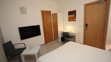 A hotel room with a bed, a desk, a chair, a TV, a mirror, and two doors.