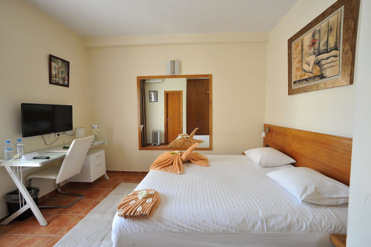 A hotel room with a bed, a desk, a chair, a television, and a painting on the wall.