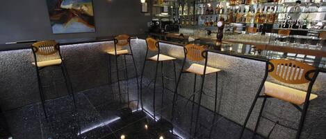 Zona de bar con taburetes altos, piso negro pulido y una pared llena de botellas de licores.