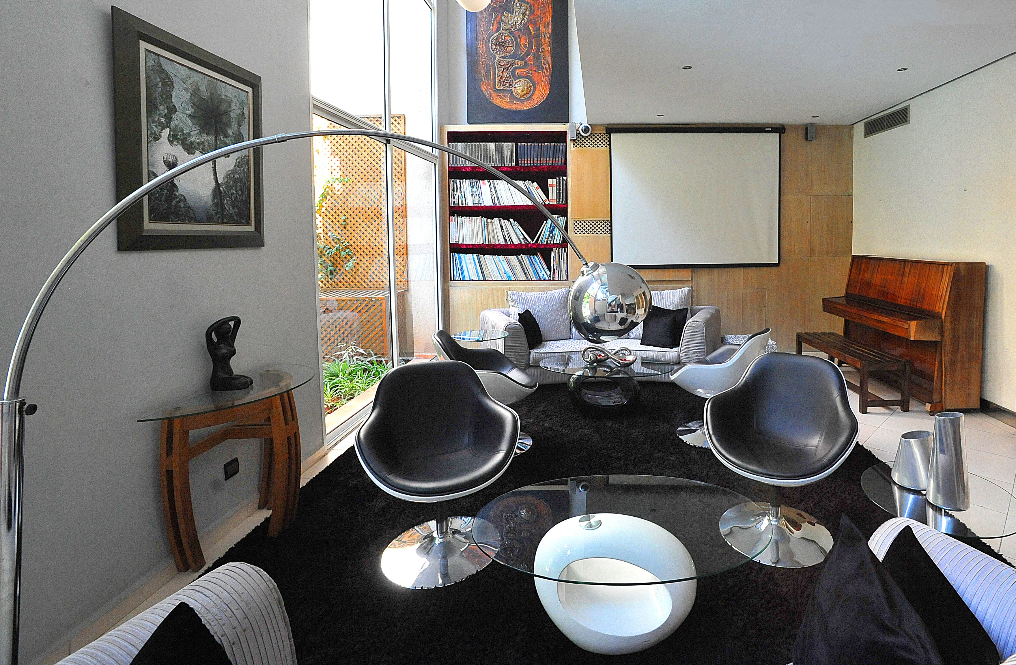 Un salon moderne avec une table basse ronde en verre, deux chaises noires, un canapé blanc et une bibliothèque.