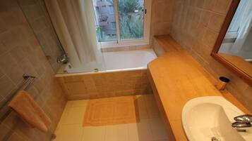 Une salle de bain avec une baignoire, un lavabo et une fenêtre donnant sur des immeubles et des palmiers.