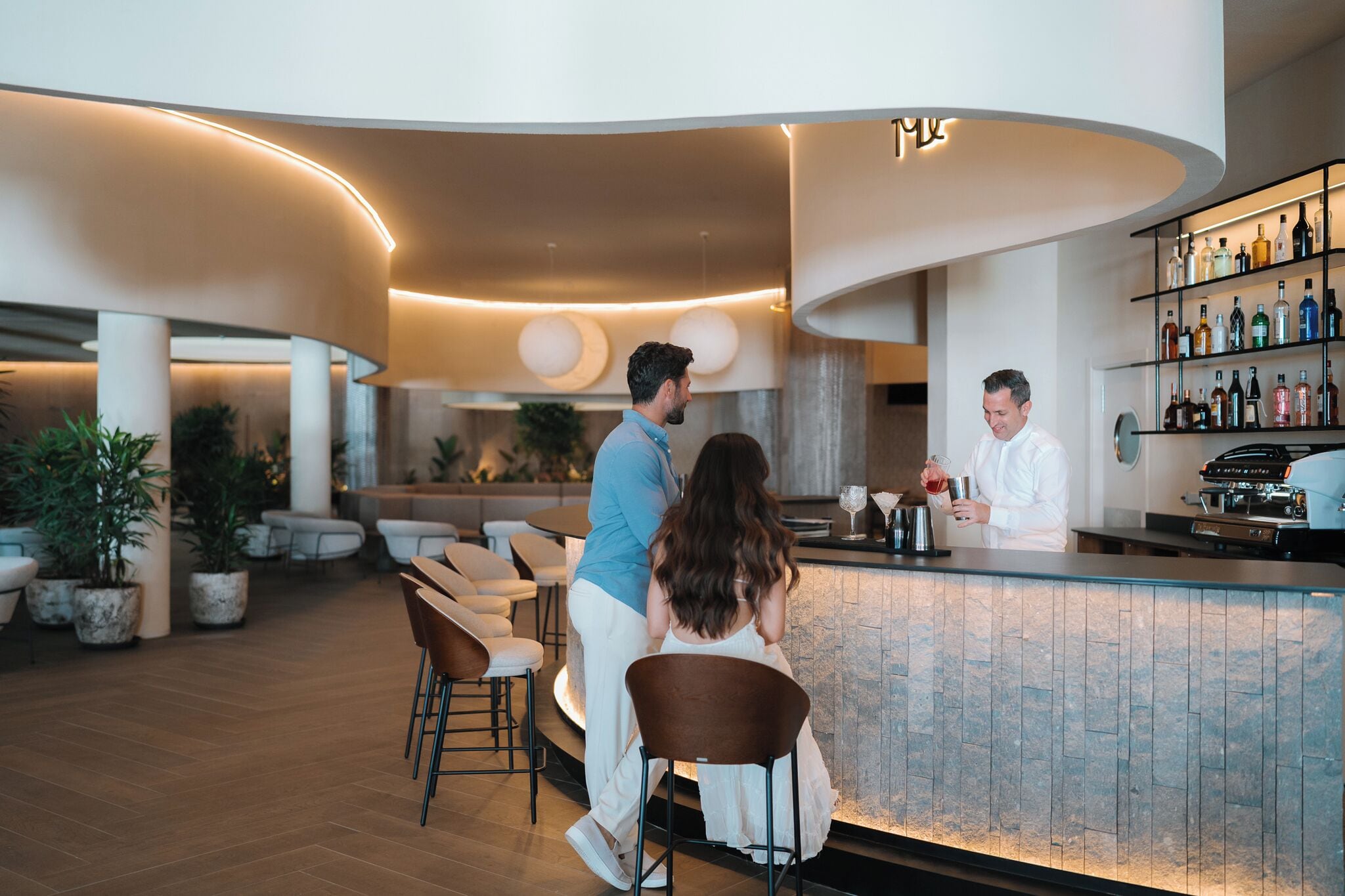 Zona de bar moderna con mostrador curvo, asientos y una barra bien surtida.