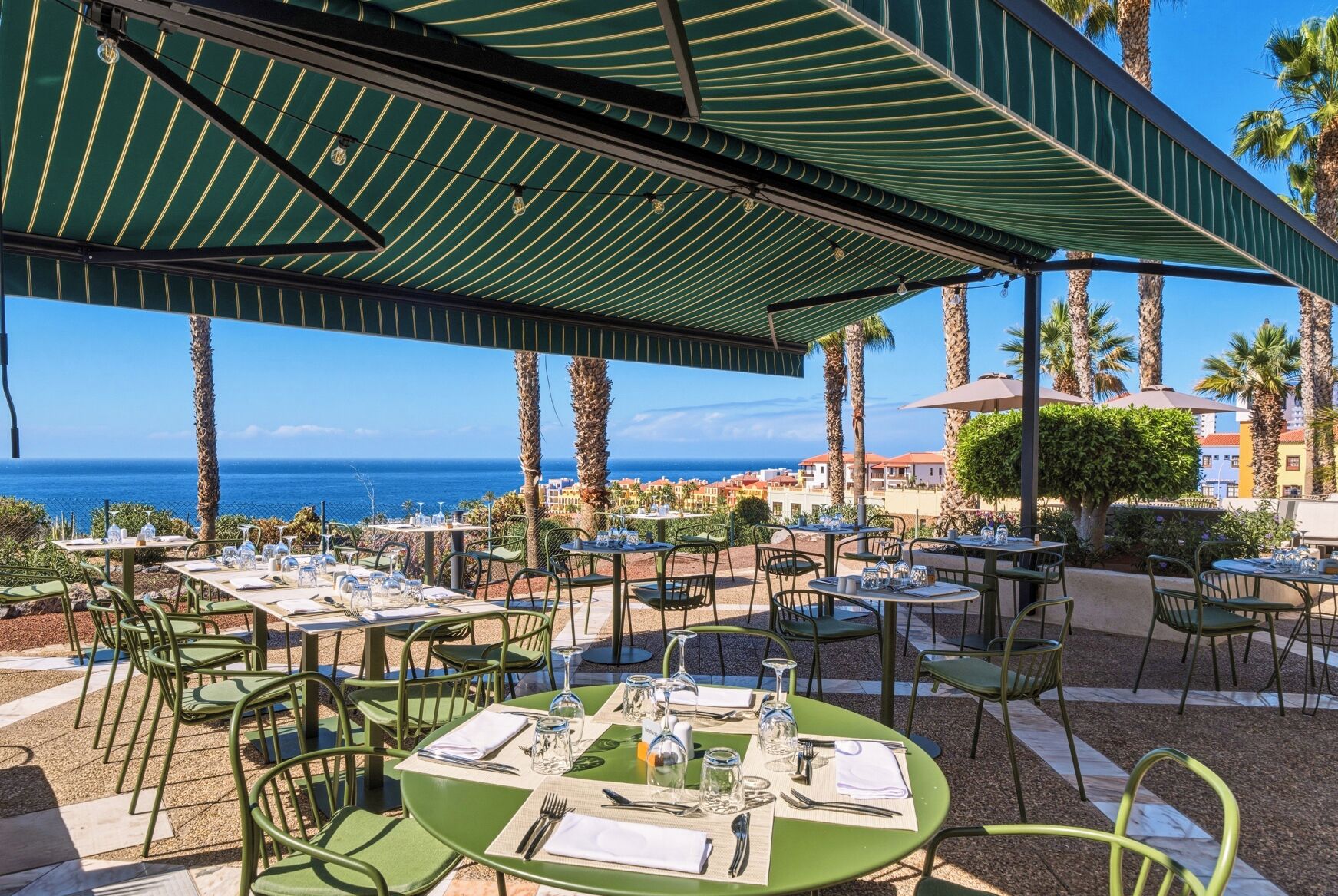 An outdoor dining area with tables and chairs, a covered patio, and a view of the ocean.