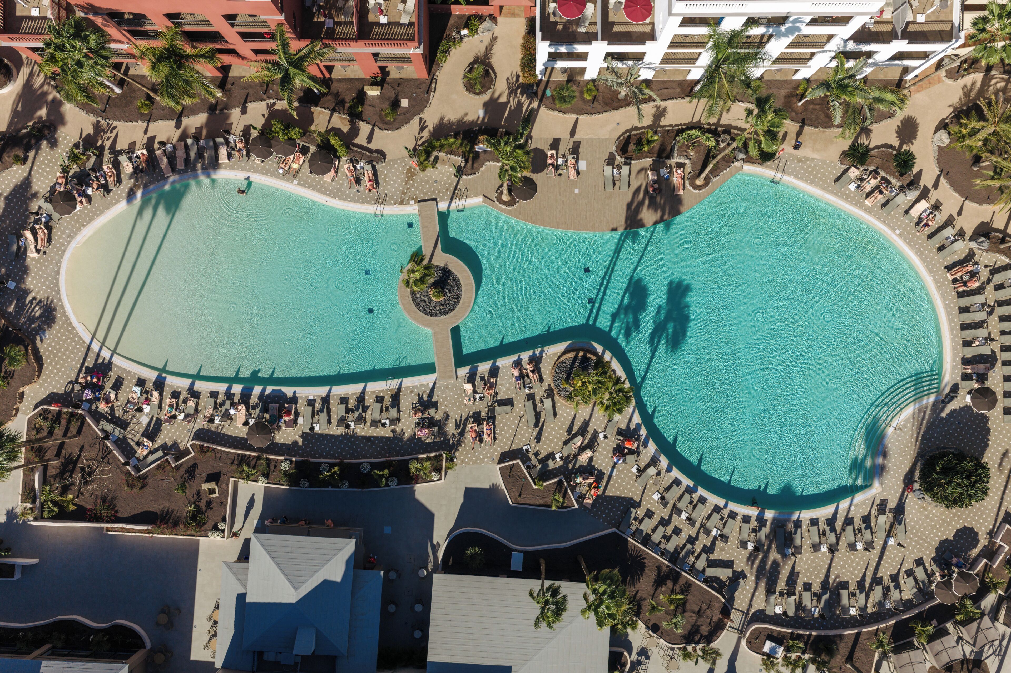 An aerial view of a resort with a large central pool, sun loungers, and palm trees.