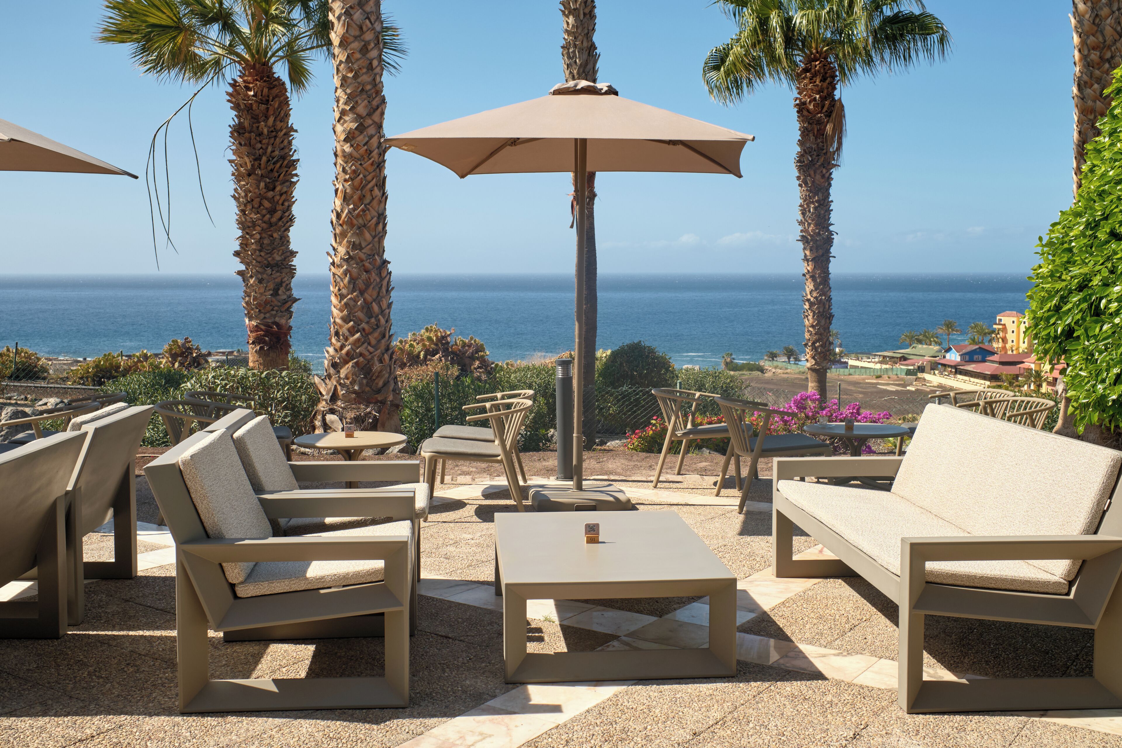 Outdoor seating with umbrellas, palm trees, and a view of the ocean.