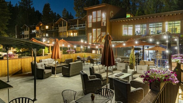 A multi-story building with outdoor seating areas, including wicker furniture and umbrellas, surrounded by trees.