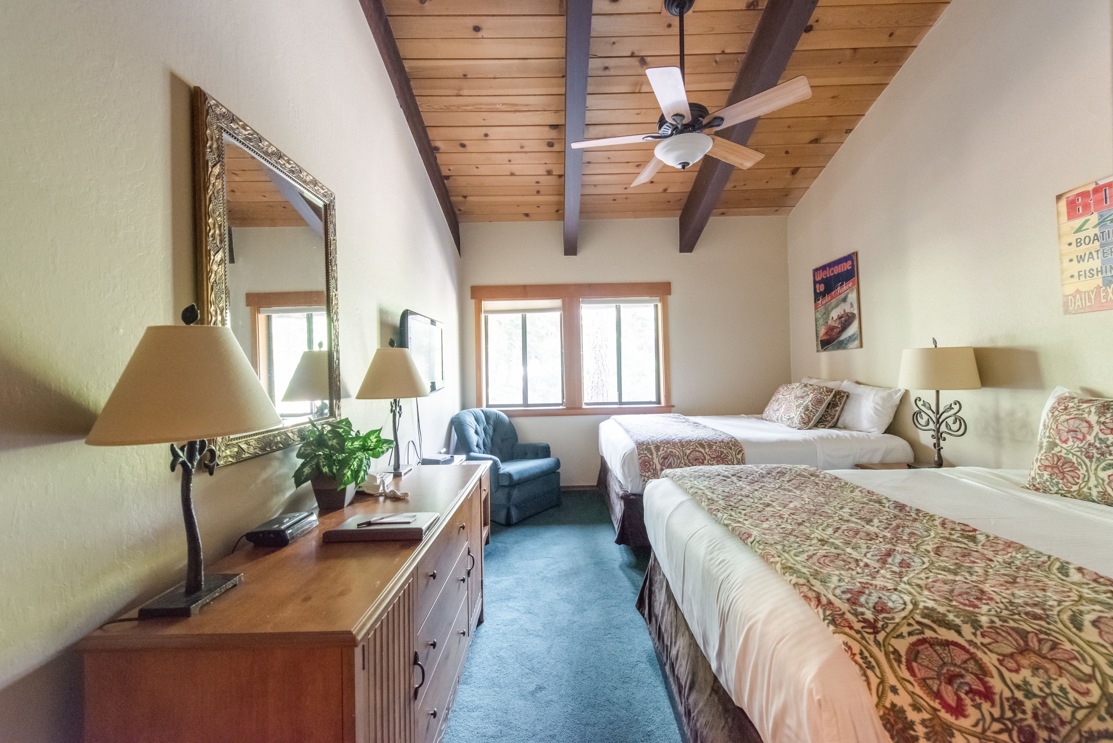 A bedroom with two beds, a ceiling fan, a large mirror, and a welcome sign.