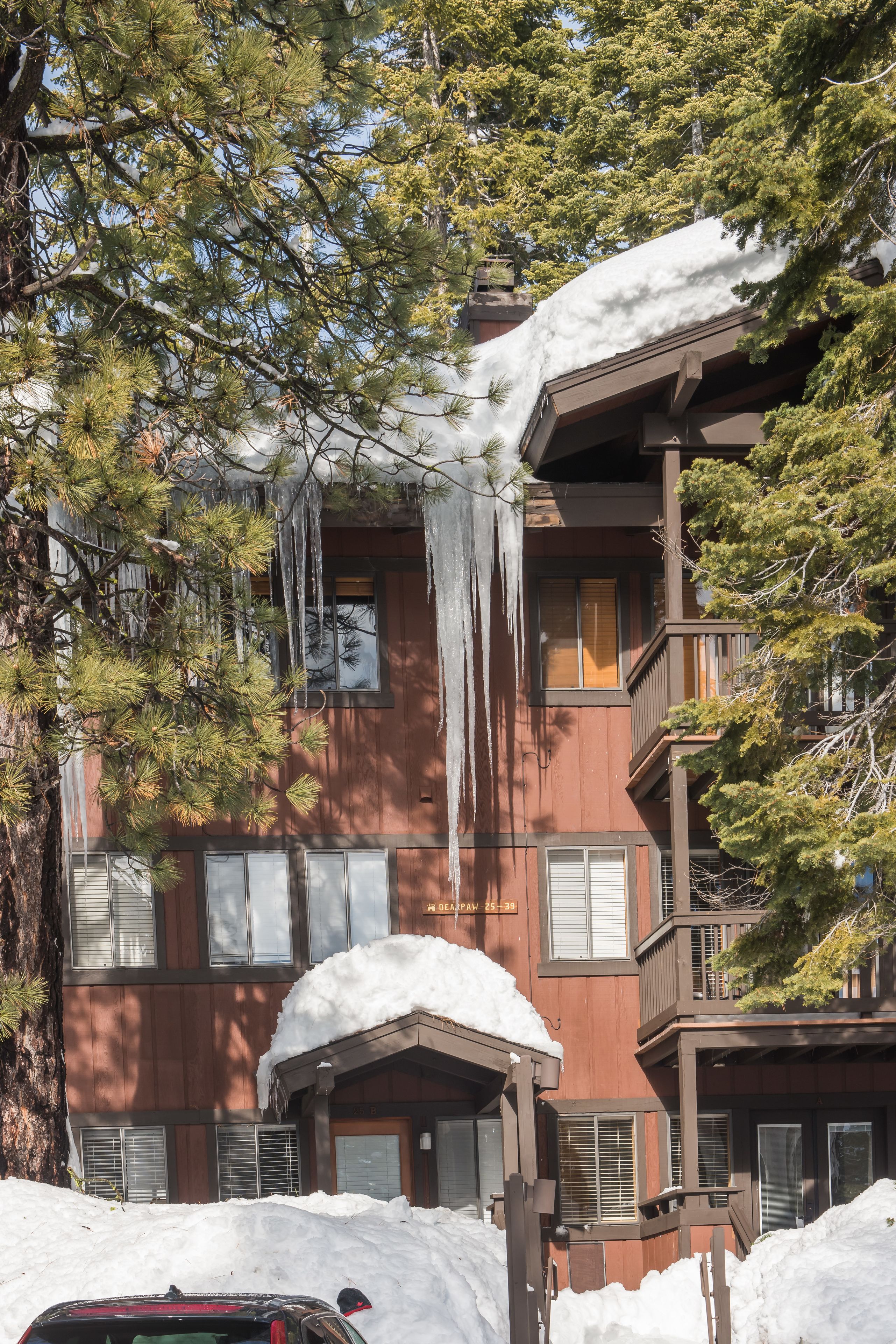Um edifício de vários andares com fachada marrom, grandes janelas e uma varanda. Há neve visível no telhado e no chão.