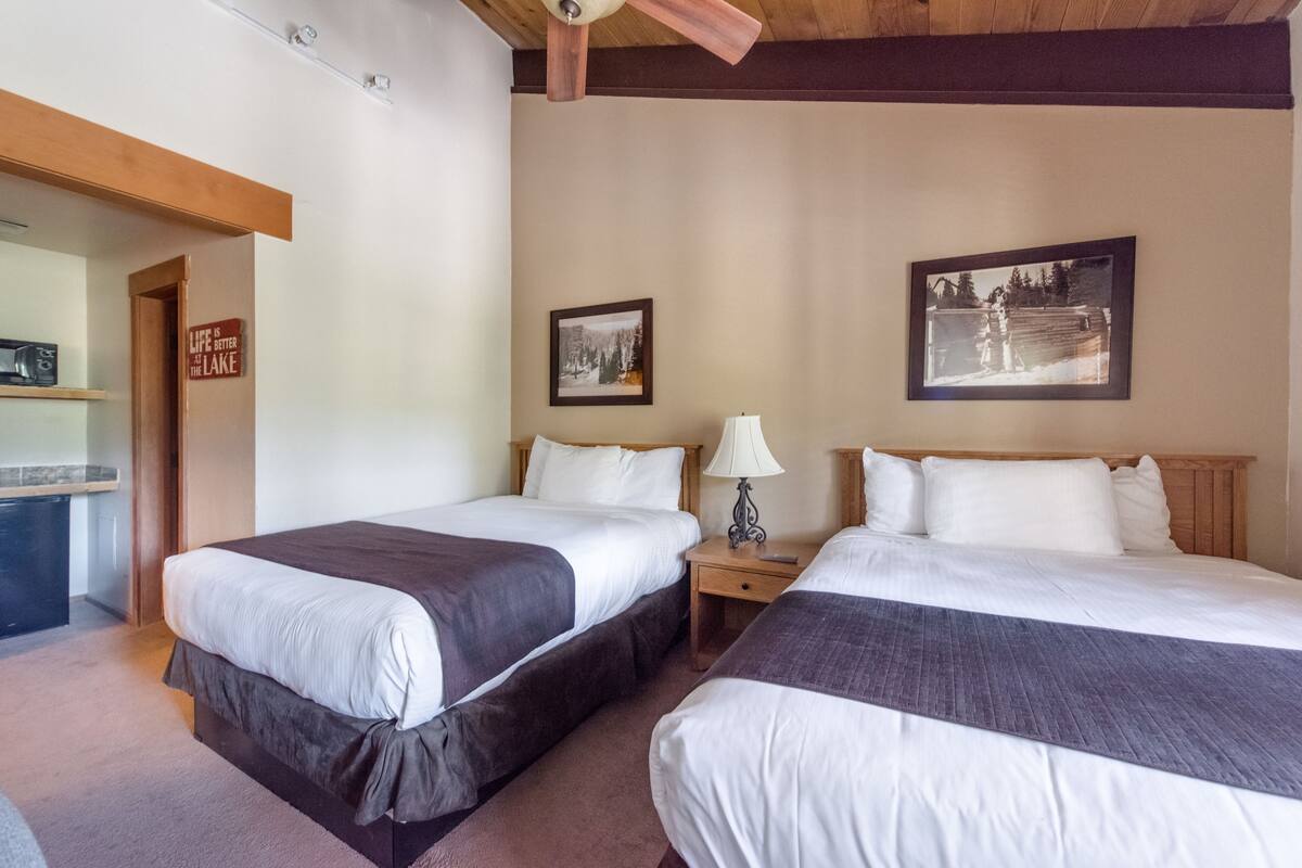 A hotel room with two beds, a nightstand with a lamp, and a wall with two framed pictures.
