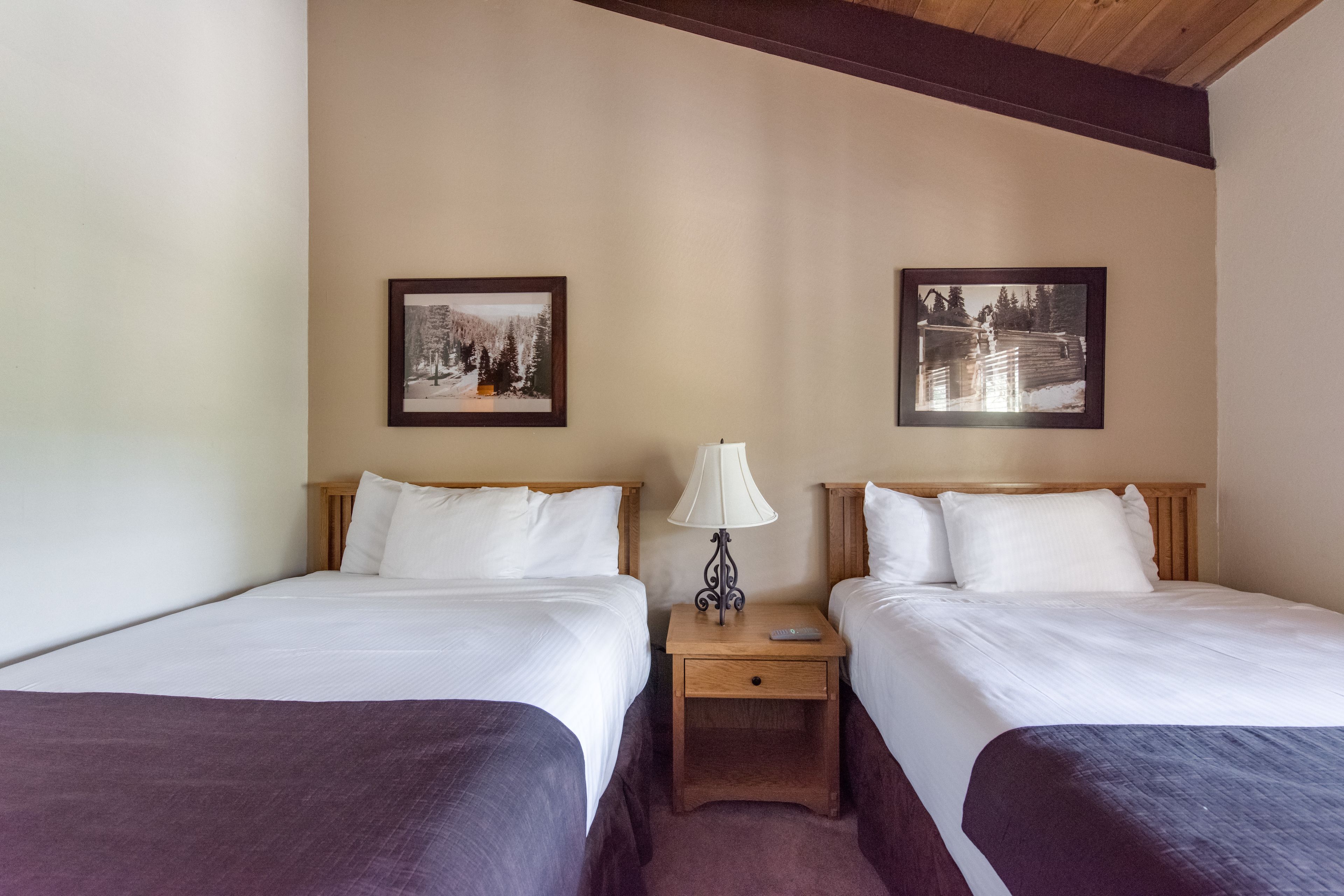 A hotel room with two beds, a nightstand with a lamp, and two framed pictures on the wall.