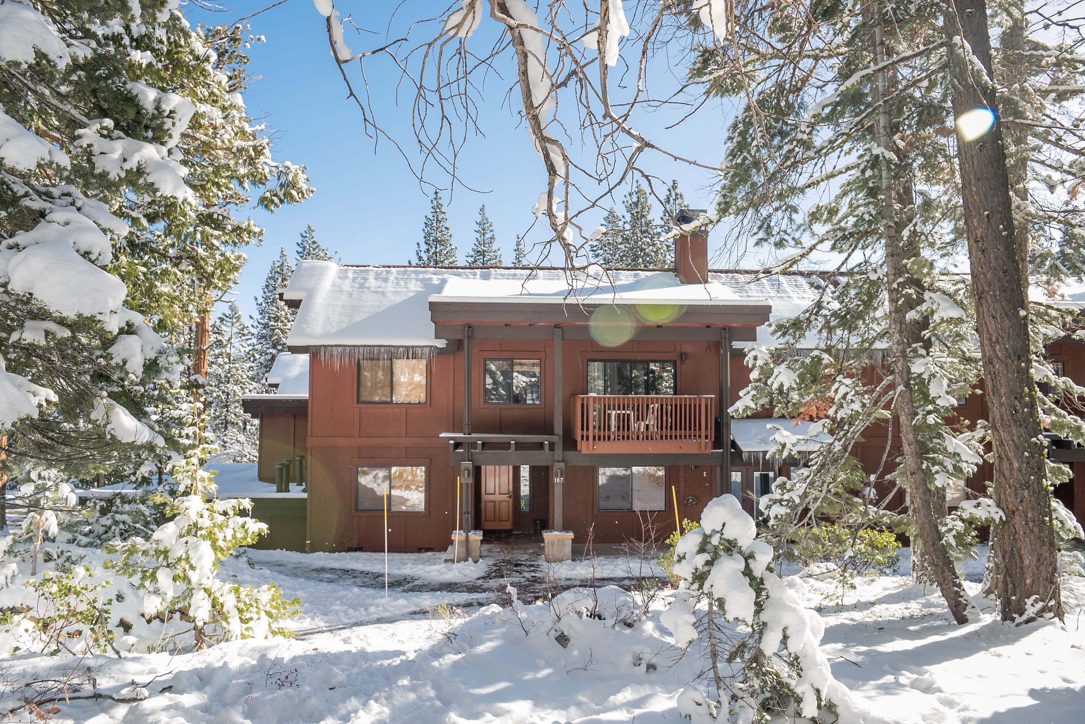A two-story wooden cabin with a balcony, surrounded by snow-covered trees.