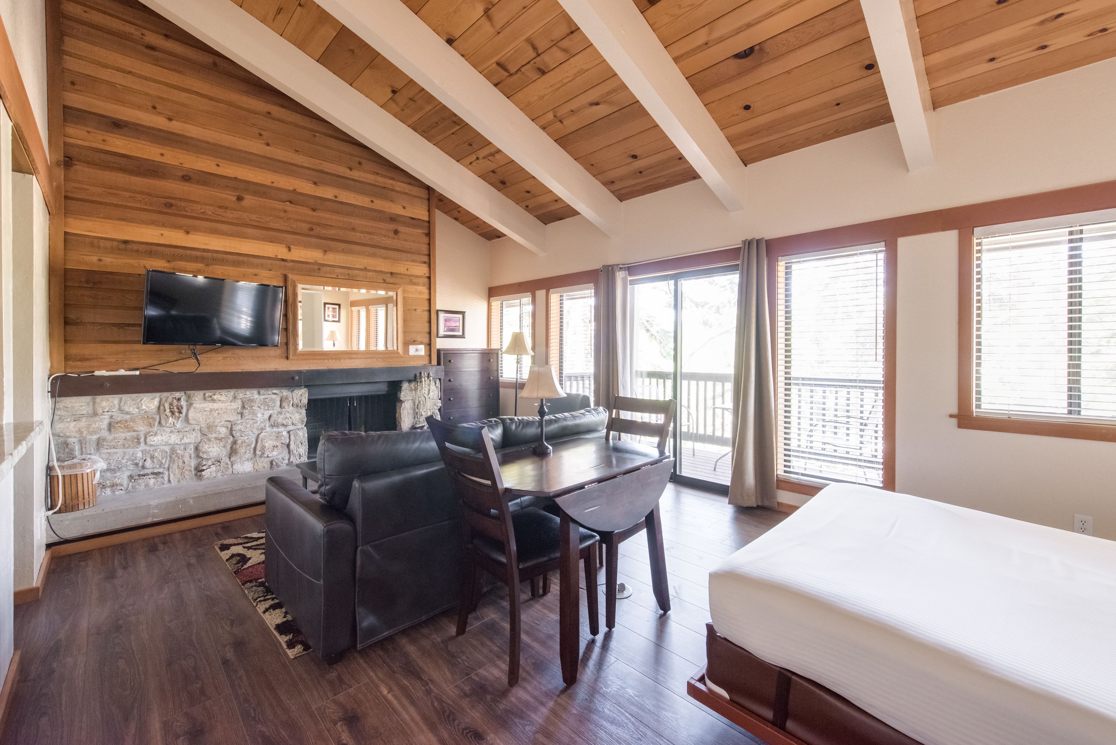 A spacious room with a stone fireplace, a black leather sofa, a dining table with chairs, and a large bed.