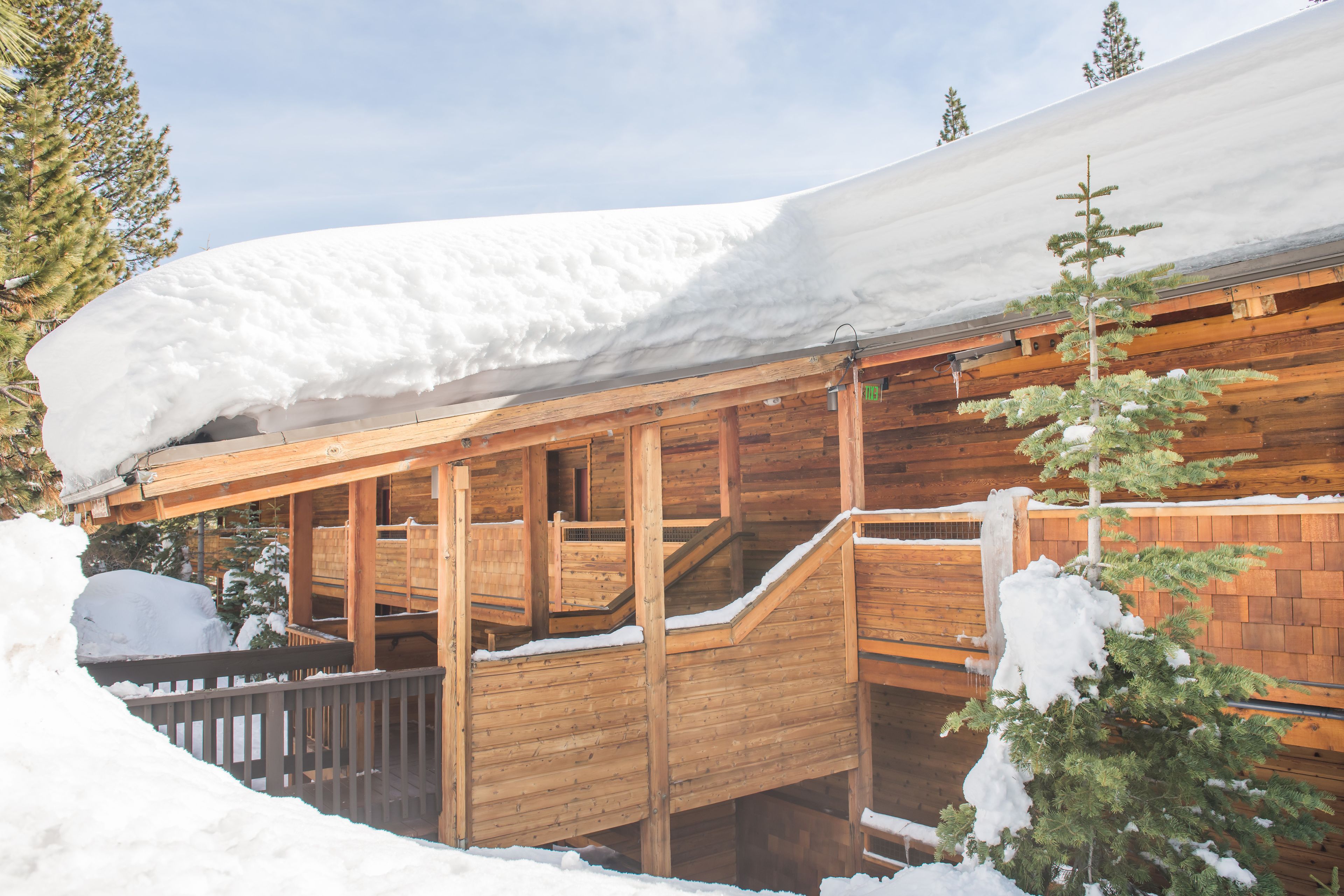 Uma cabana de madeira com telhado coberto de neve e escadaria de madeira que leva à entrada.