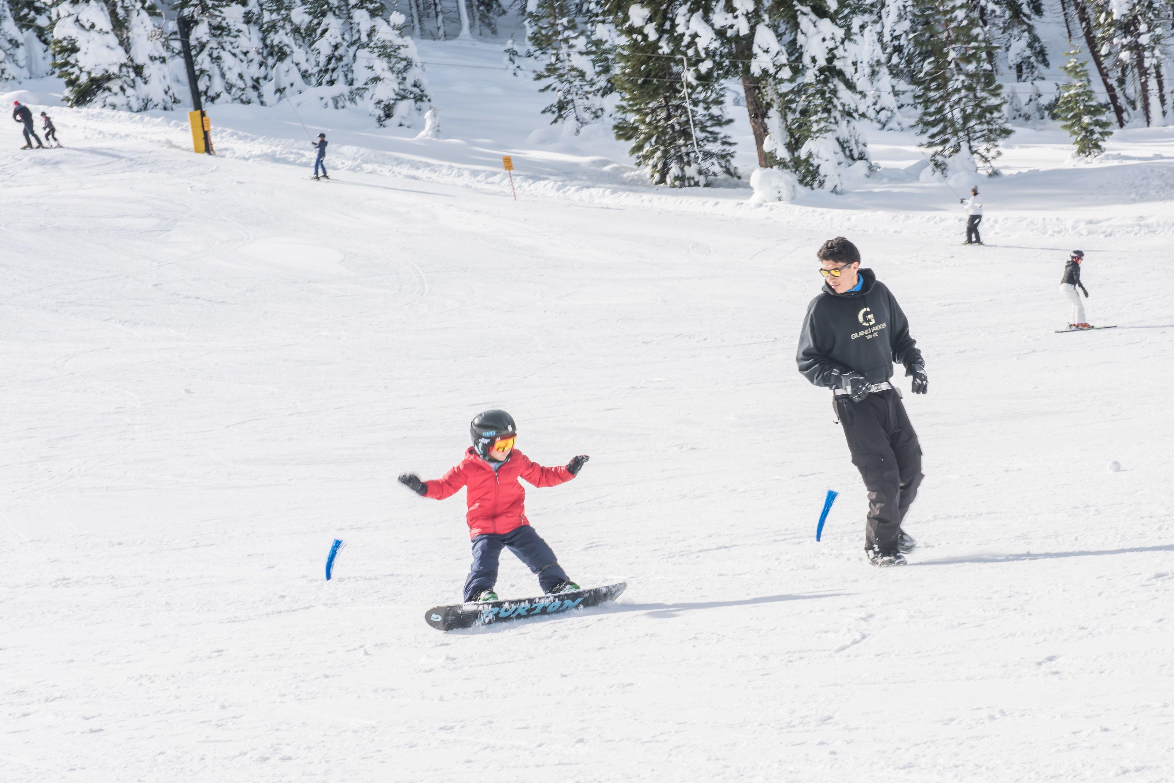 A snowy ski slope with skiers and a child on a snowboard.