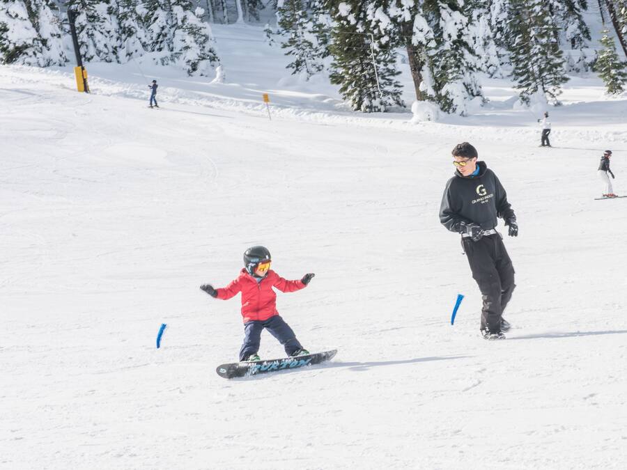 A snowy ski slope with skiers and a child on a snowboard.