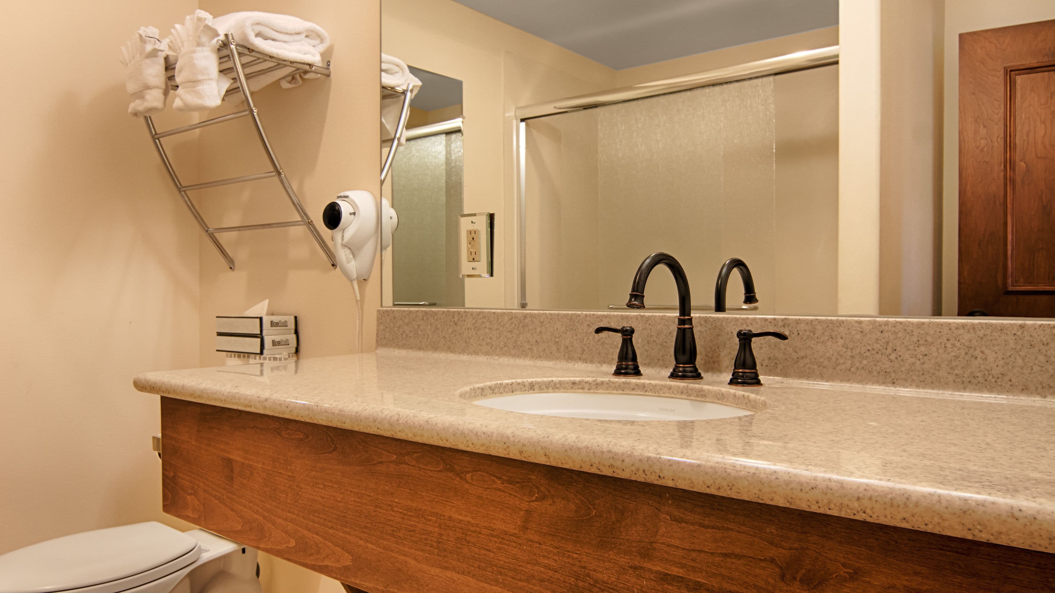 A bathroom with a sink, two faucets, a towel rack with towels, a hairdryer, and a mirror.