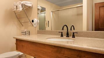 A bathroom with a sink, two faucets, a towel rack with towels, a hairdryer, and a mirror.