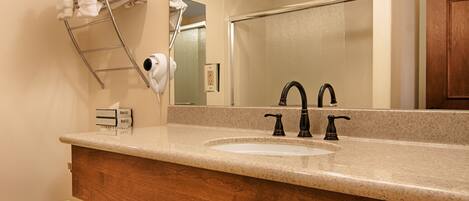 A bathroom with a sink, two faucets, a towel rack with towels, a hairdryer, and a mirror.