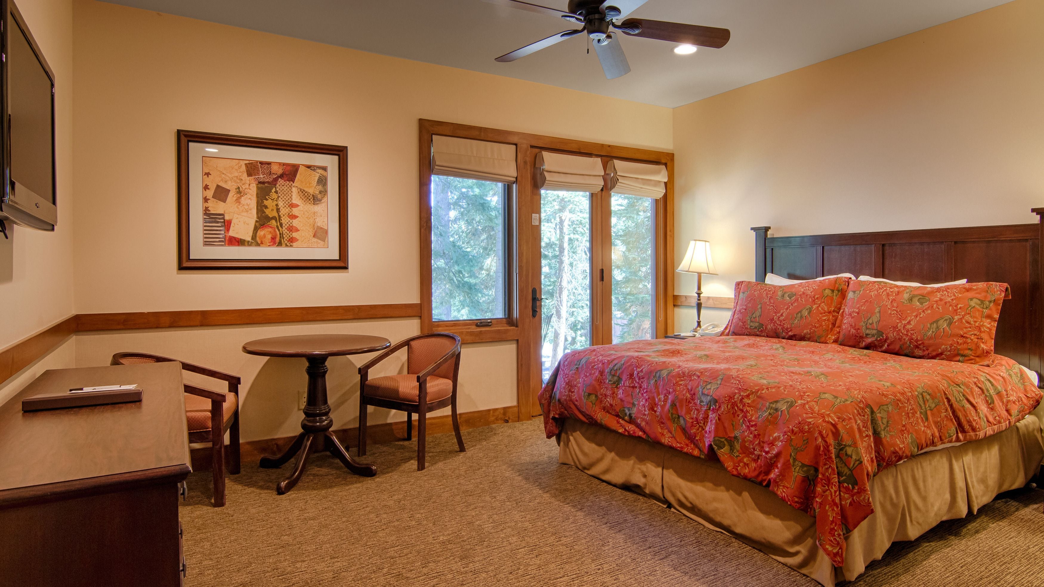 A hotel room with a bed, a desk, a chair, a framed picture on the wall, and a window with a view of trees.