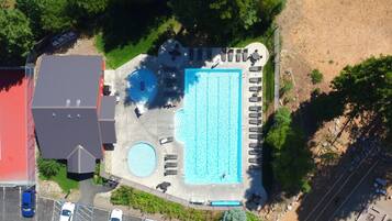 An aerial view of a property with a large swimming pool, a covered area, and a parking lot.
