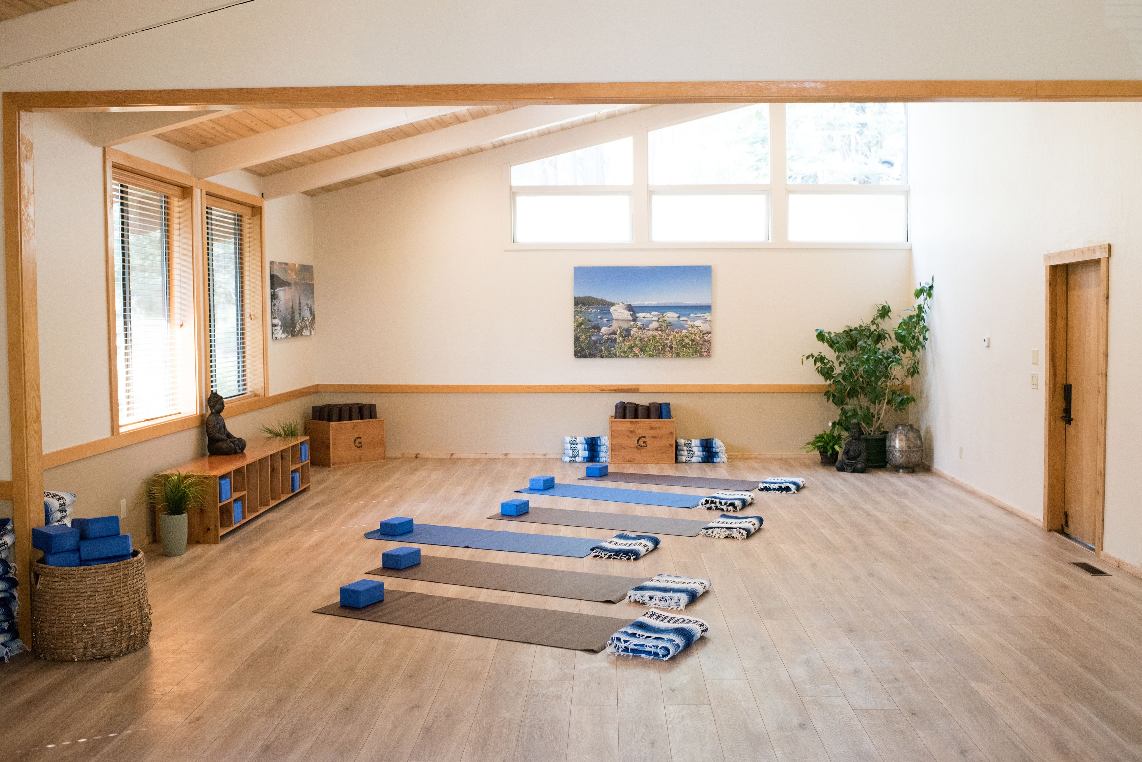 Amplia habitación con pisos de madera, un ventanal grande y vista al mar. Se observan colchonetas y bloques de yoga dispuestos para hacer ejercicio.
