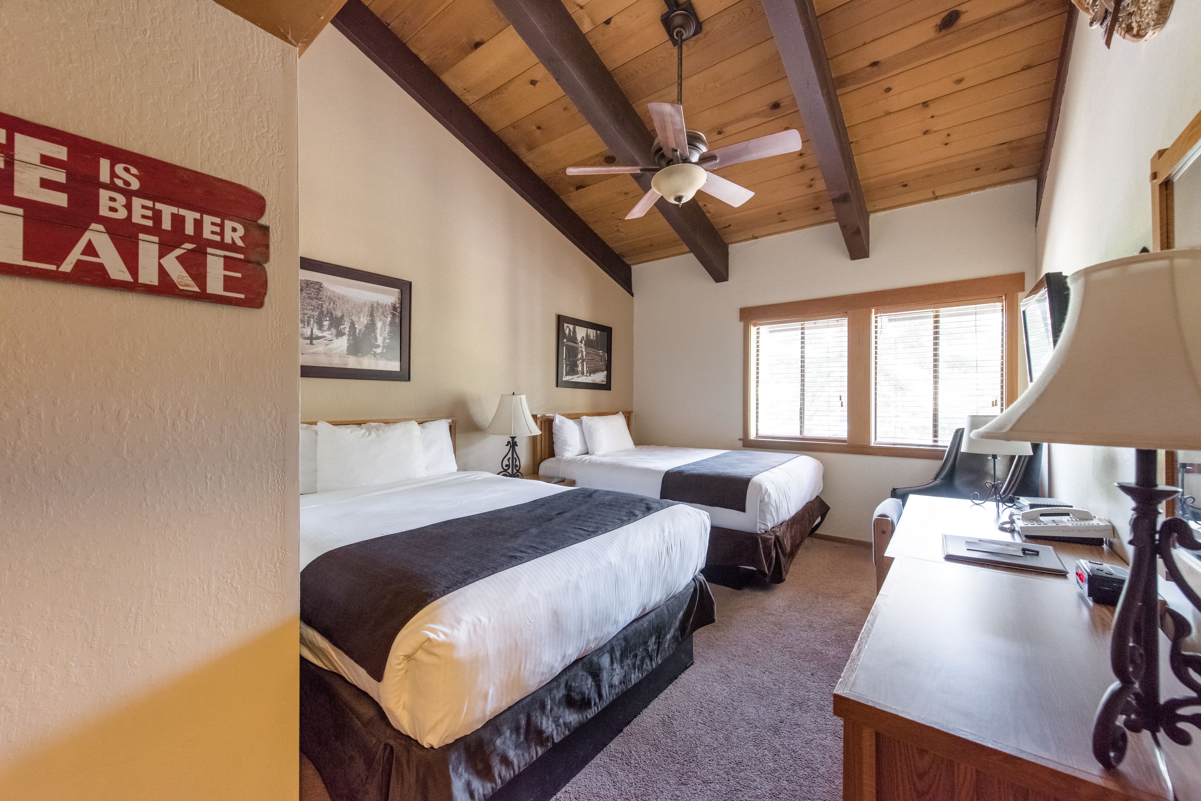 A hotel room with two beds, a desk, a ceiling fan, and a sign on the wall.