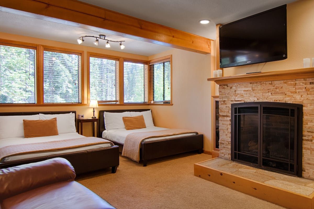 A bedroom with two beds, a fireplace, and a TV mounted on the wall.