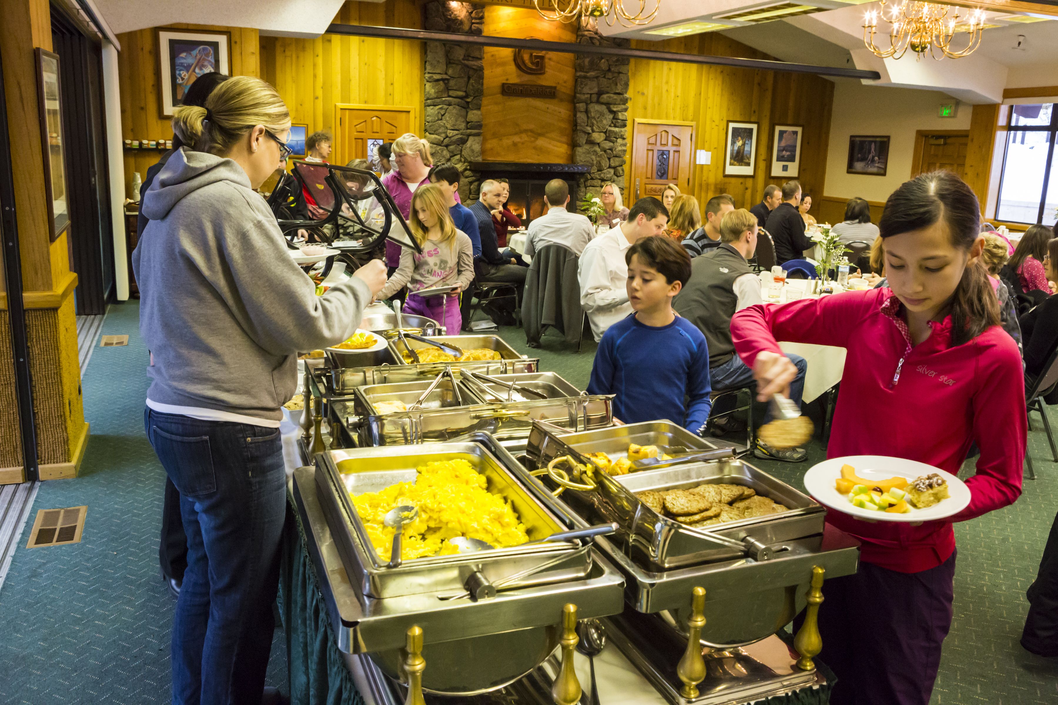 A buffet setup with multiple food service stations, a stone wall, and a chandelier.