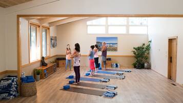 Clase de yoga en una habitación con suelo de madera, ventanas amplias y vistas a un paisaje urbano.