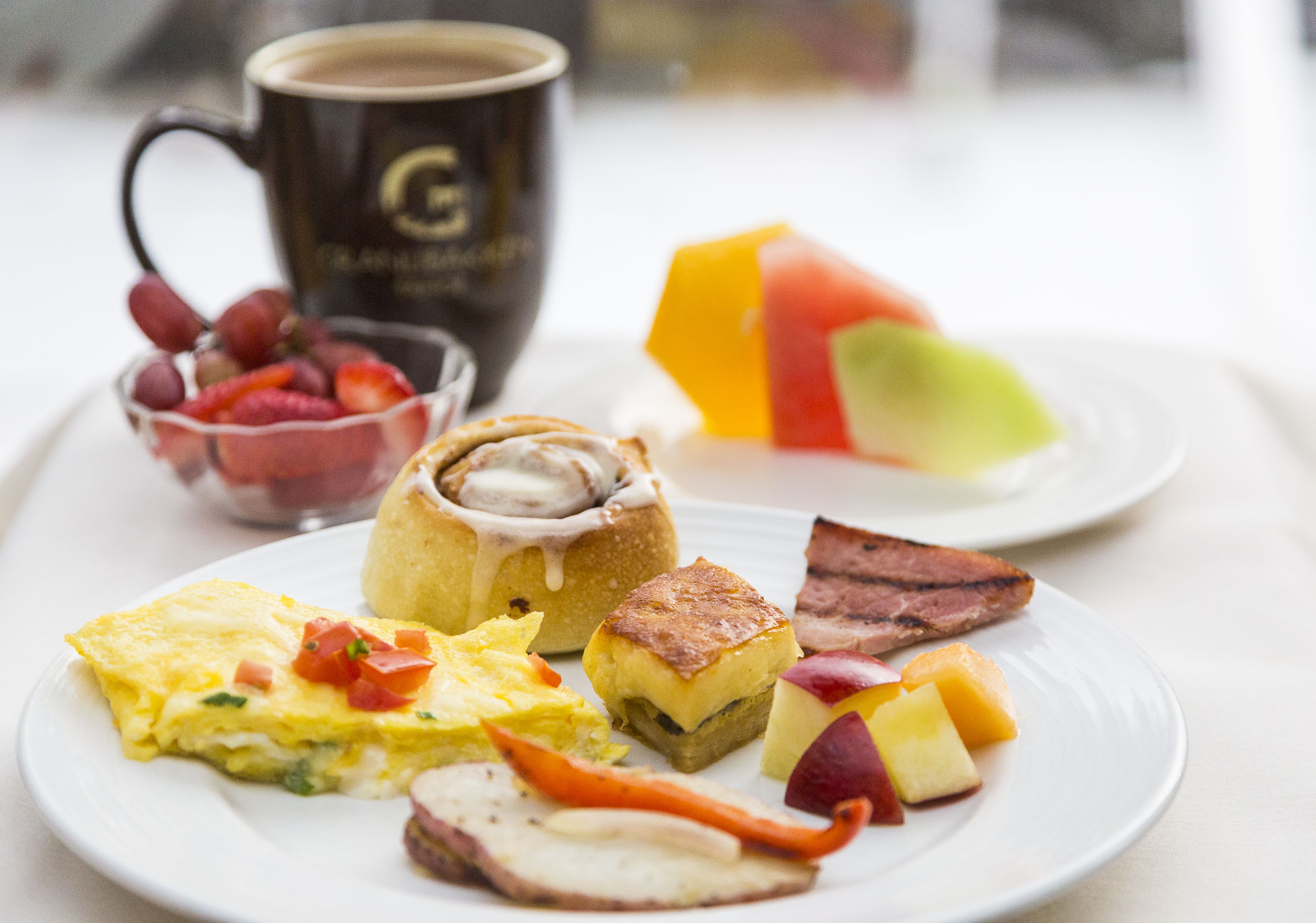 Een ontbijt bord met eieren, spek, toast, fruit en een koffiemok.
