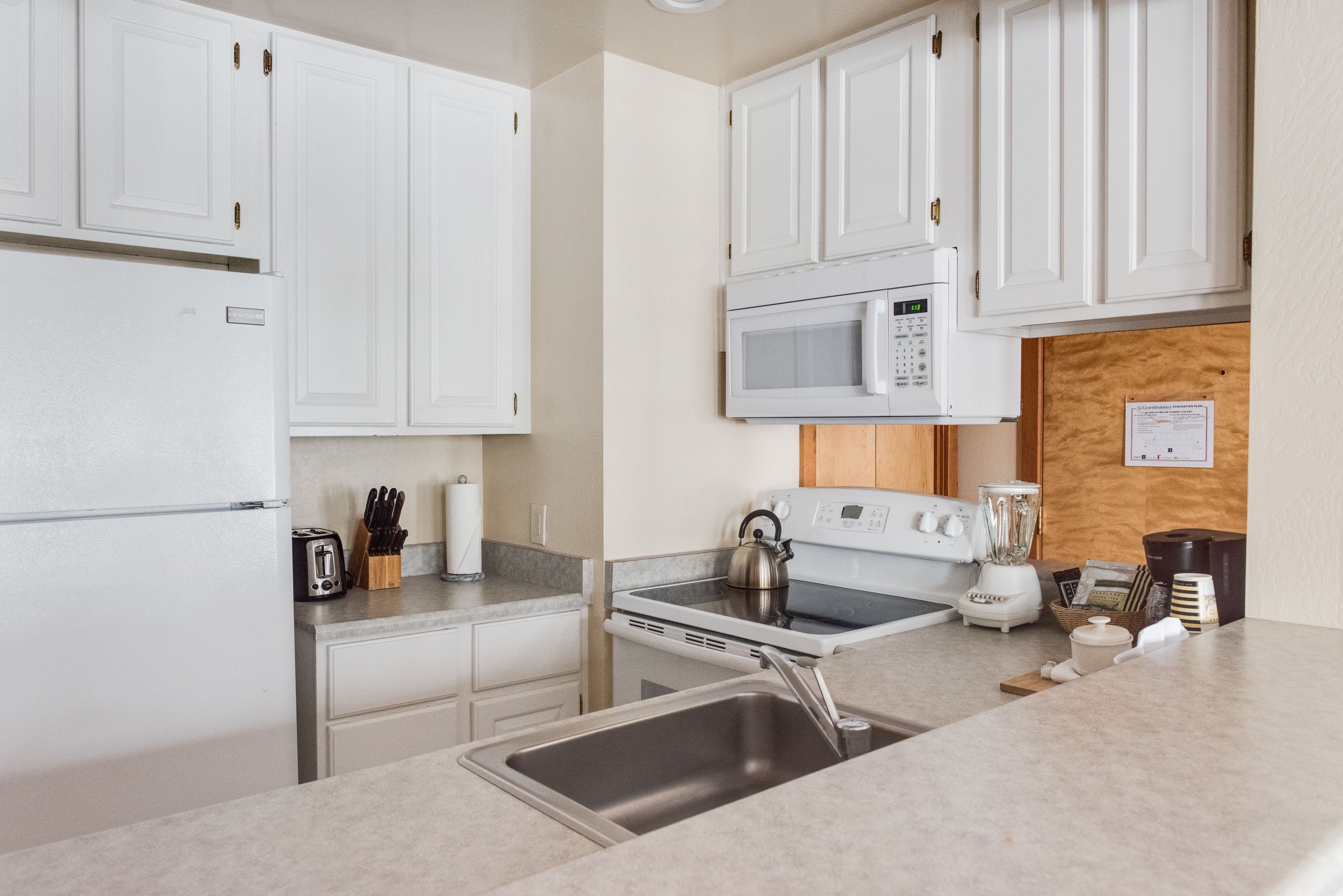 A modern kitchen with white cabinets, a built-in microwave, a stove, and a sink.