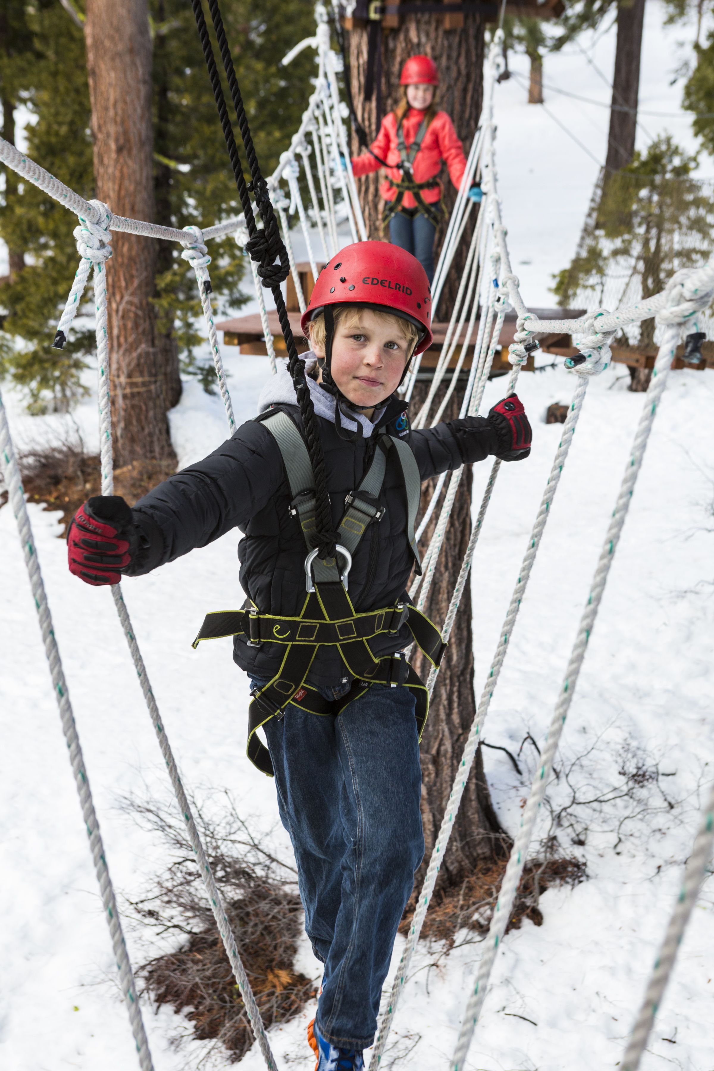 A person on a rope bridge in a snowy forest.