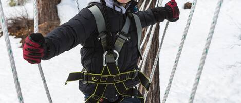 A person on a rope bridge in a snowy forest.