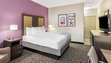 Quarto de hotel com cama, escrivaninha, cadeira, televisão e obras de arte na parede.