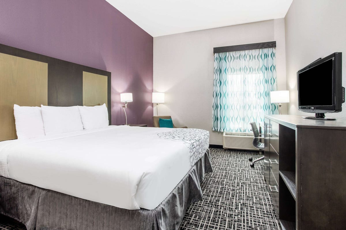 Habitación de hotel con una cama grande, un escritorio con televisor y una ventana con cortinas estampadas.
