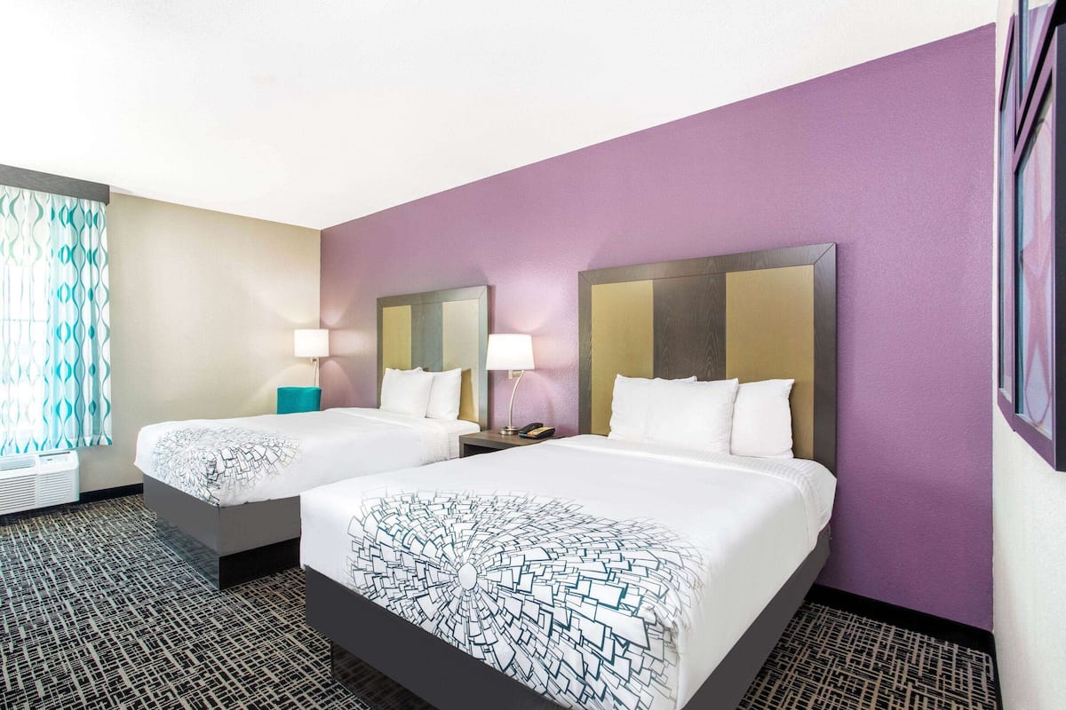 Habitación de hotel con dos camas, alfombra estampada y paredes moradas.