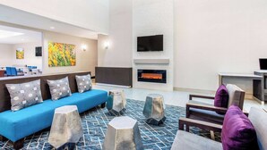 A modern lobby with a blue sofa, patterned cushions, a fireplace, and a flat-screen TV mounted on the wall. - La Quinta Inn & Suites by Wyndham Hillsboro (Hillsboro)
