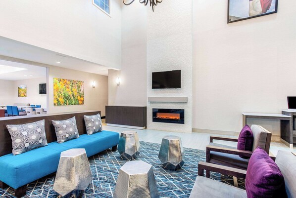 A modern lobby with a blue sofa, patterned cushions, a fireplace, and a flat-screen TV mounted on the wall. - La Quinta Inn & Suites by Wyndham Hillsboro (Hillsboro)