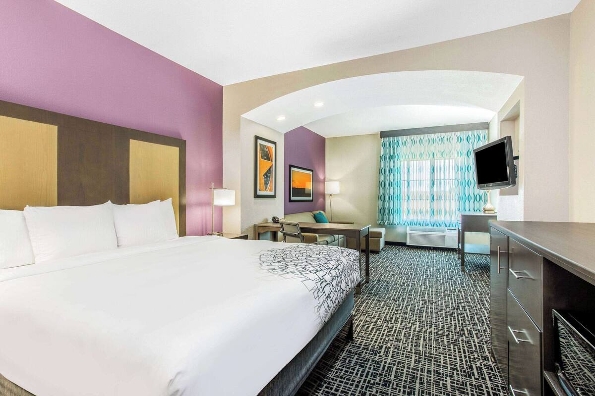 Una habitación de hotel con una cama grande, un escritorio, una silla, un televisor y una ventana con cortinas.