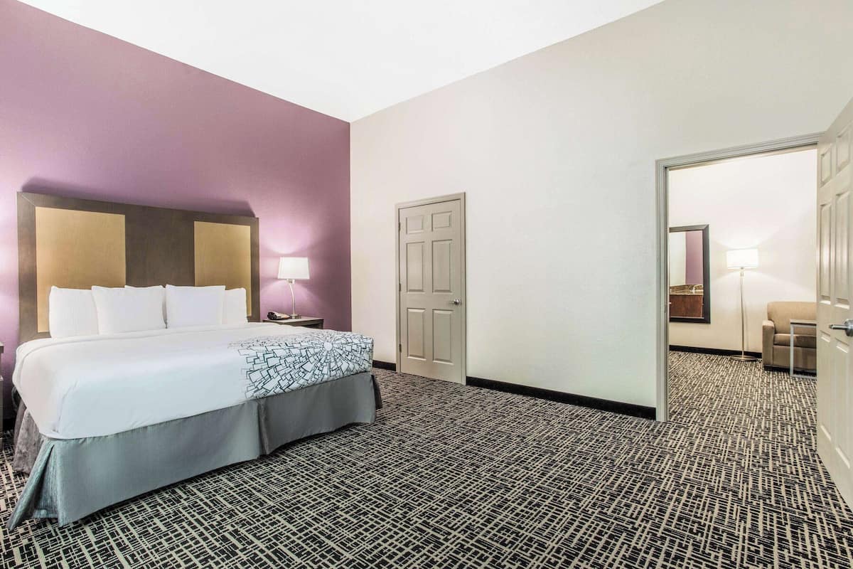 Una habitación de hotel con una cama grande, una mesita de noche, una lámpara, una puerta y un pequeño rincón de descanso.