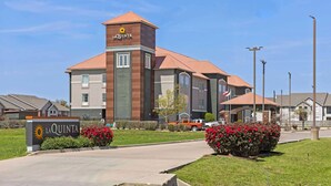 A La Quinta hotel with a prominent sign, a red-tiled roof, and a landscaped entrance with red flowers. - La Quinta Inn & Suites by Wyndham Hillsboro (Hillsboro)